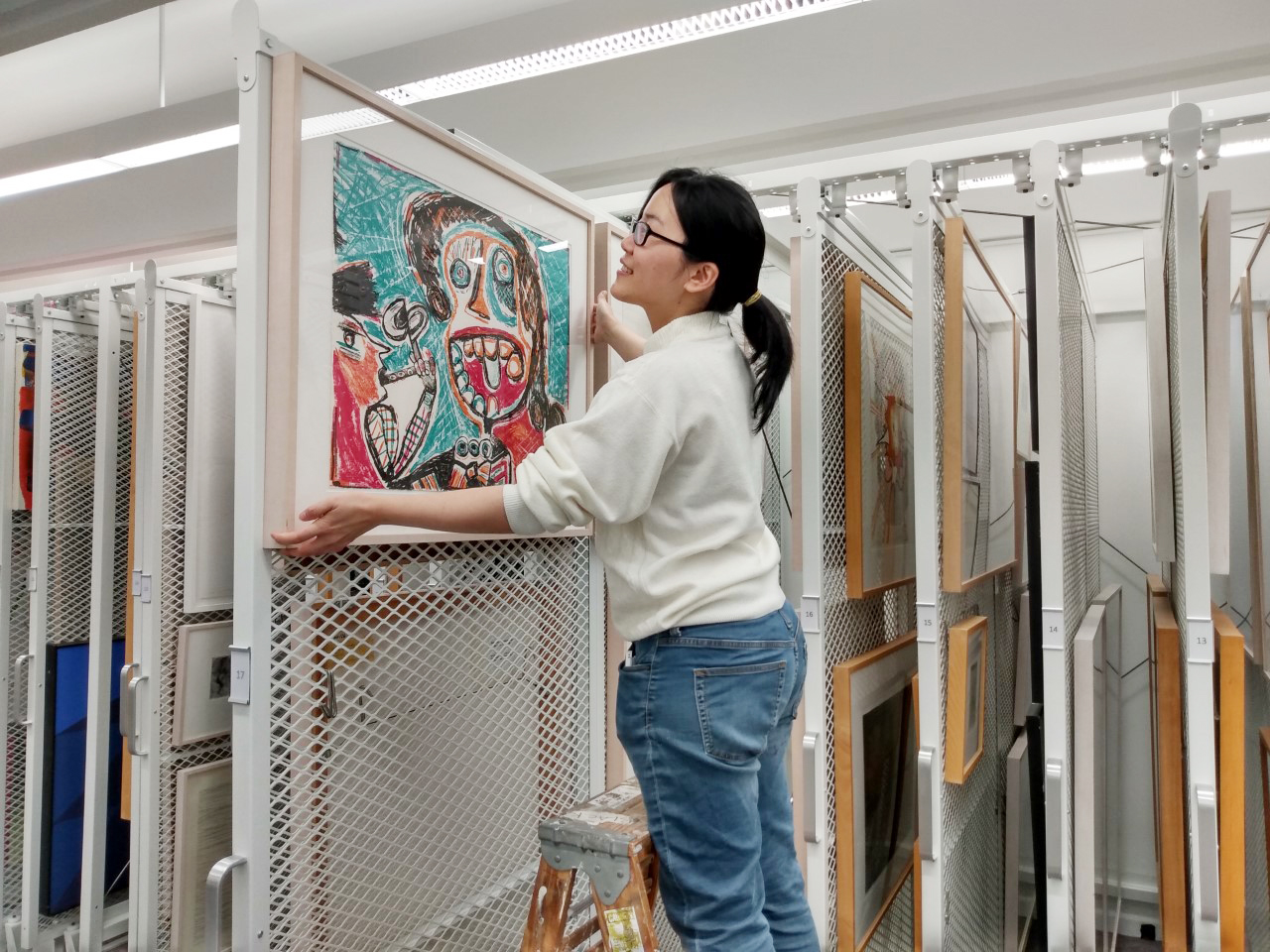 A young woman on a ladder in front of a display of artwork on sliding library walls